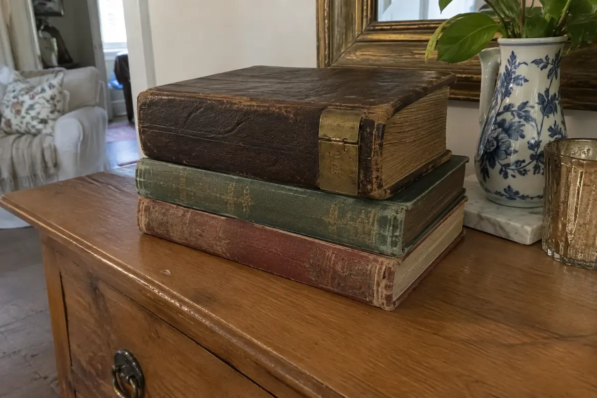 Stack of old leather and cloth-bound books, including a family Bible with a brass clasp, on a wooden sideboard