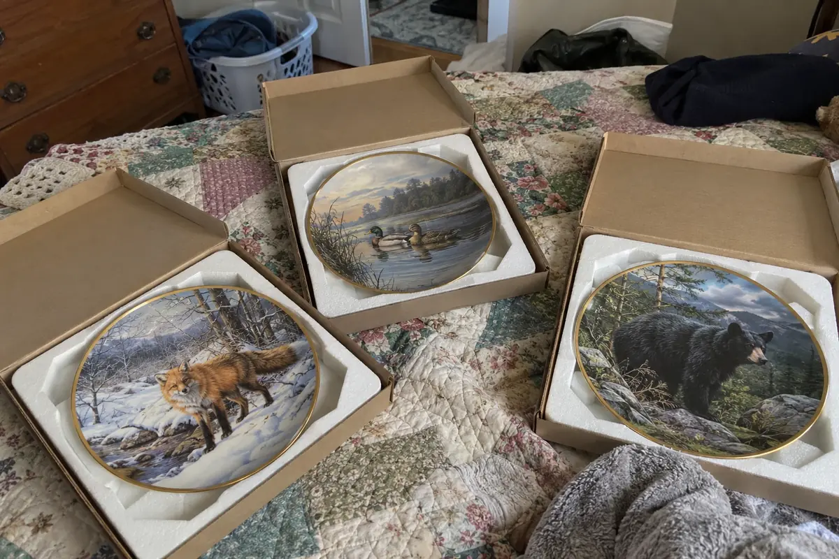 Three boxed collector plates with wildlife scenes on a quilt