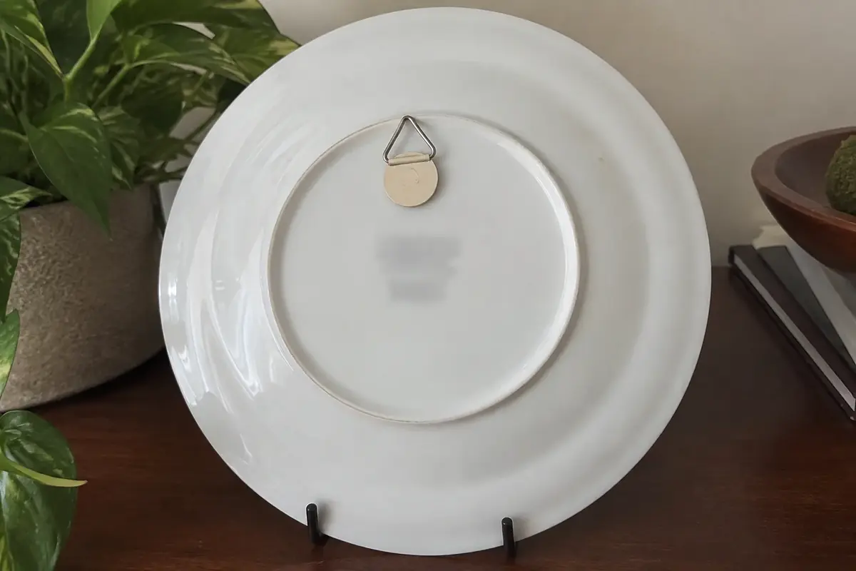 Back of a porcelain collector plate showing a white glazed base, foot ring and a block of small printed lines