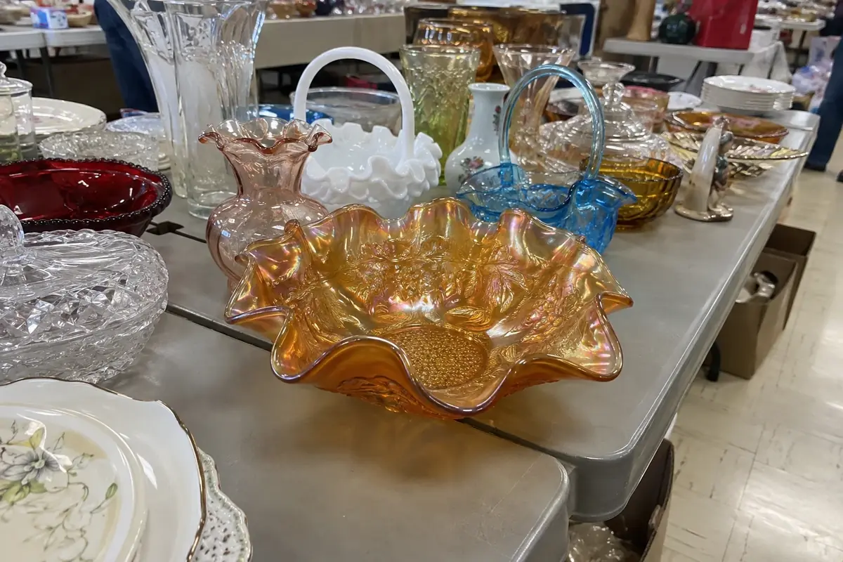 A marigold carnival glass bowl with a ruffled rim on an estate-sale table