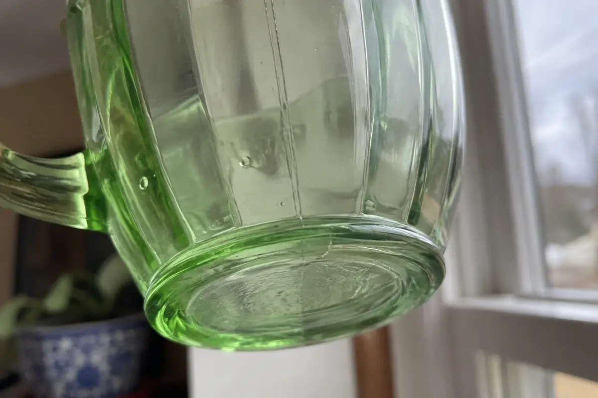 Underside of a green depression glass cup showing a faint mold seam and tiny air bubbles
