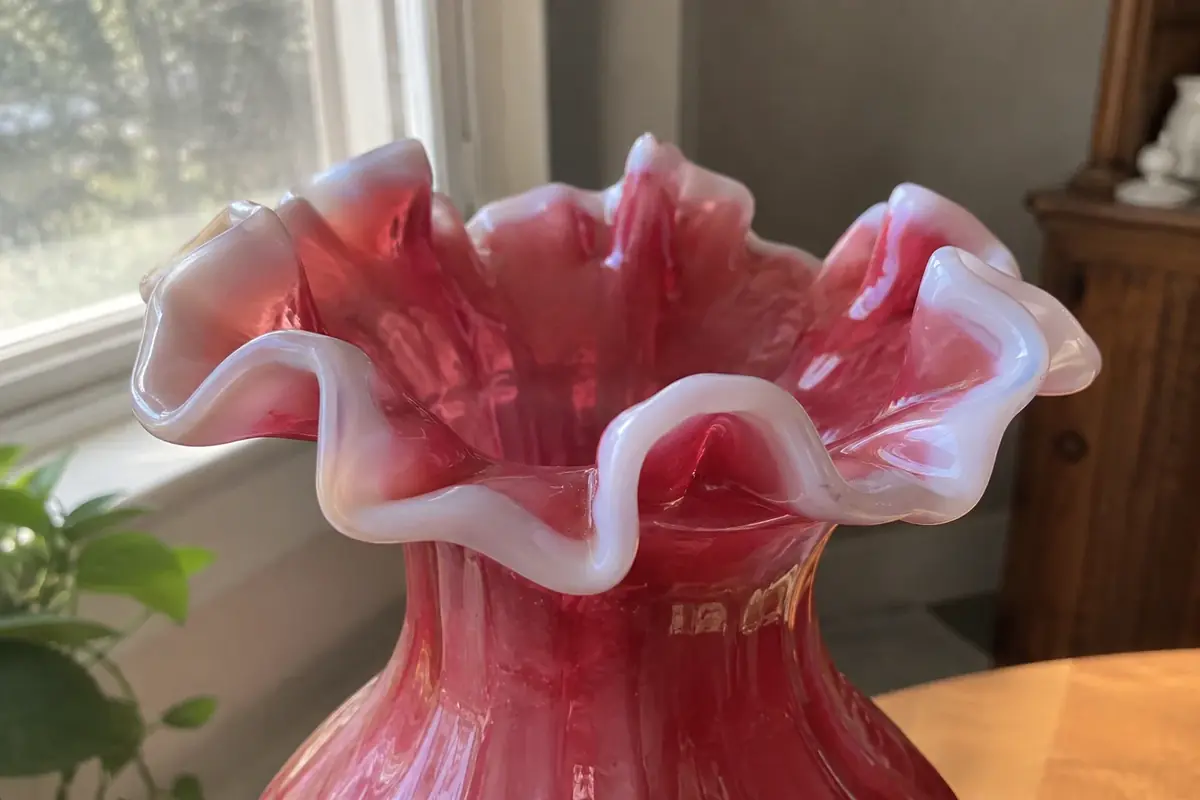 Close view of a cranberry opalescent glass vase rim with a milky white edge and uneven hand-crimped ruffles