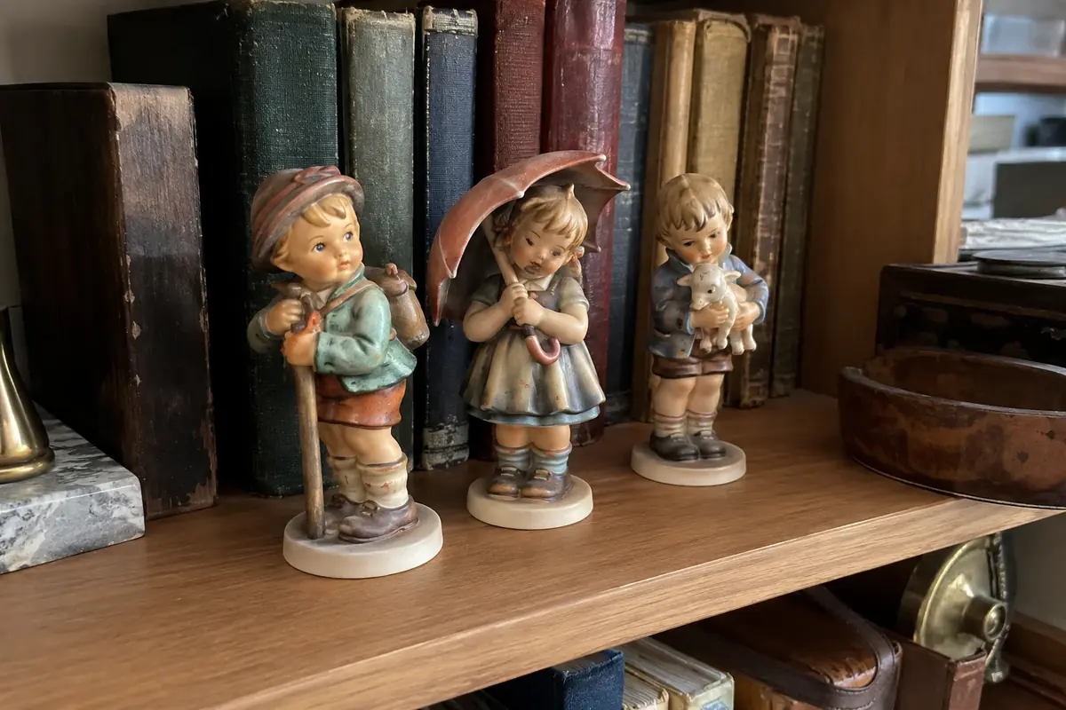 Three Goebel Hummel figurines of children on a bookshelf