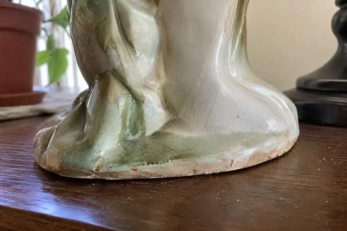 Close view of a ceramic figurine's base rim and glaze in side light, showing fine surface crazing