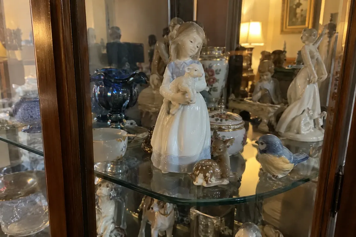 A pale blue and white porcelain figurine of a girl with a lamb inside a glass curio cabinet