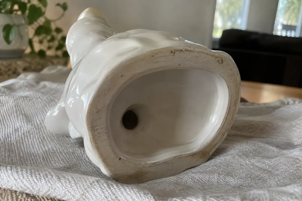Underside of a glazed porcelain figurine on a soft cloth, showing the unglazed rim and small vent hole