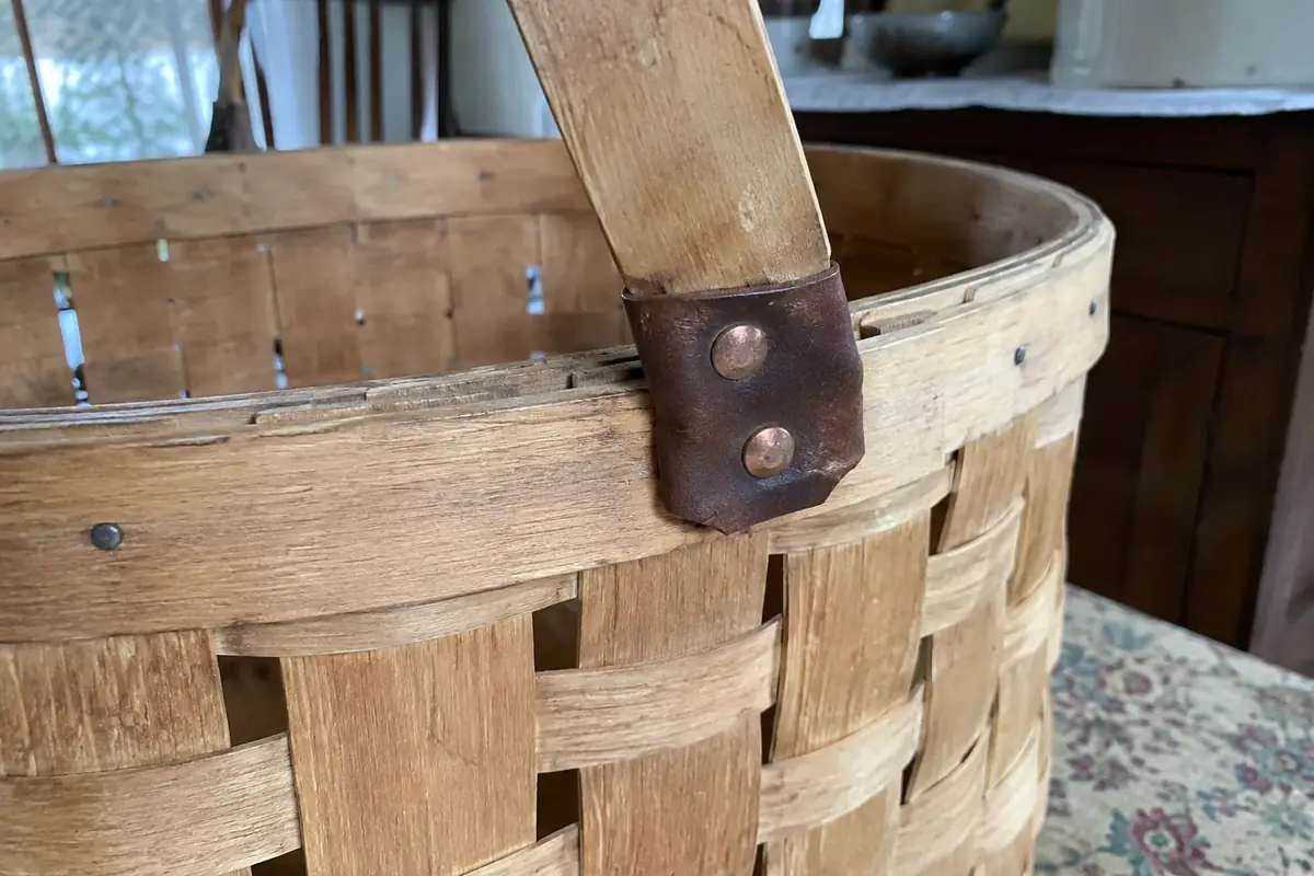 Close-up of a basket rim with small tacks, a leather handle hinge and copper rivets