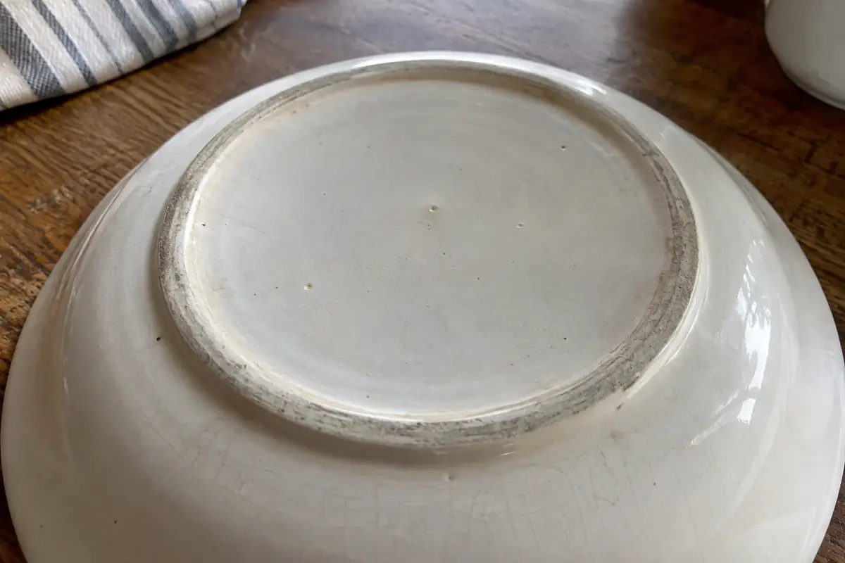 Underside of a white ceramic plate showing an unglazed foot ring, wear ring and fine crazing in raking light