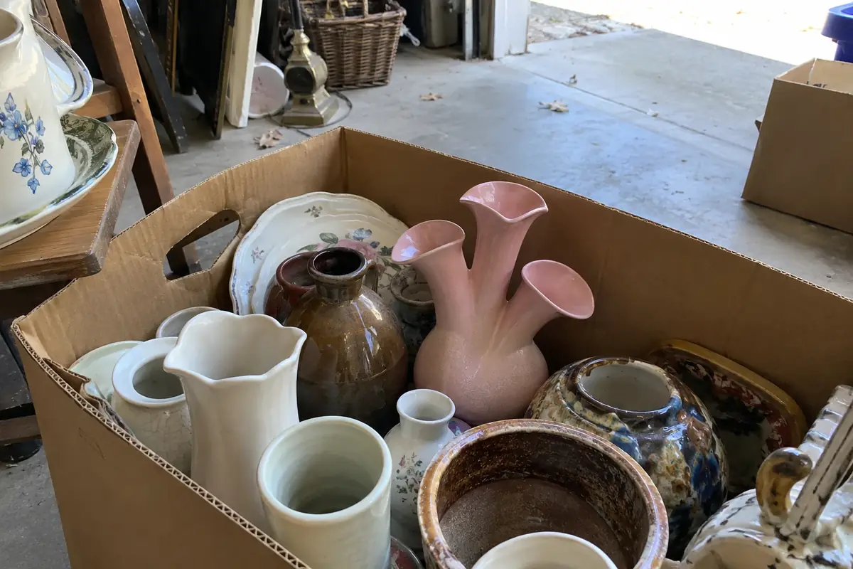 A pink triple calla-lily pottery vase in a box of mixed pottery at a garage sale