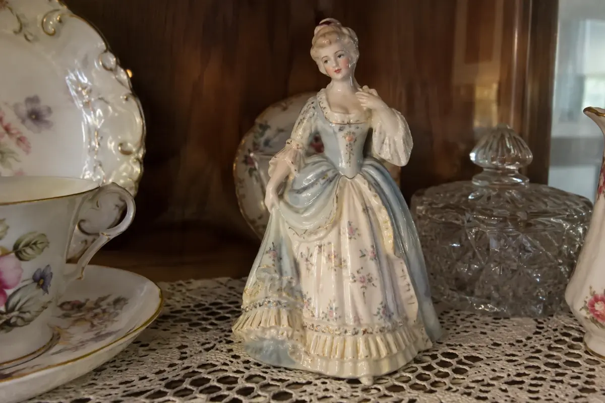 Hand-painted porcelain lady figurine in a pastel gown on a lace doily in a china cabinet