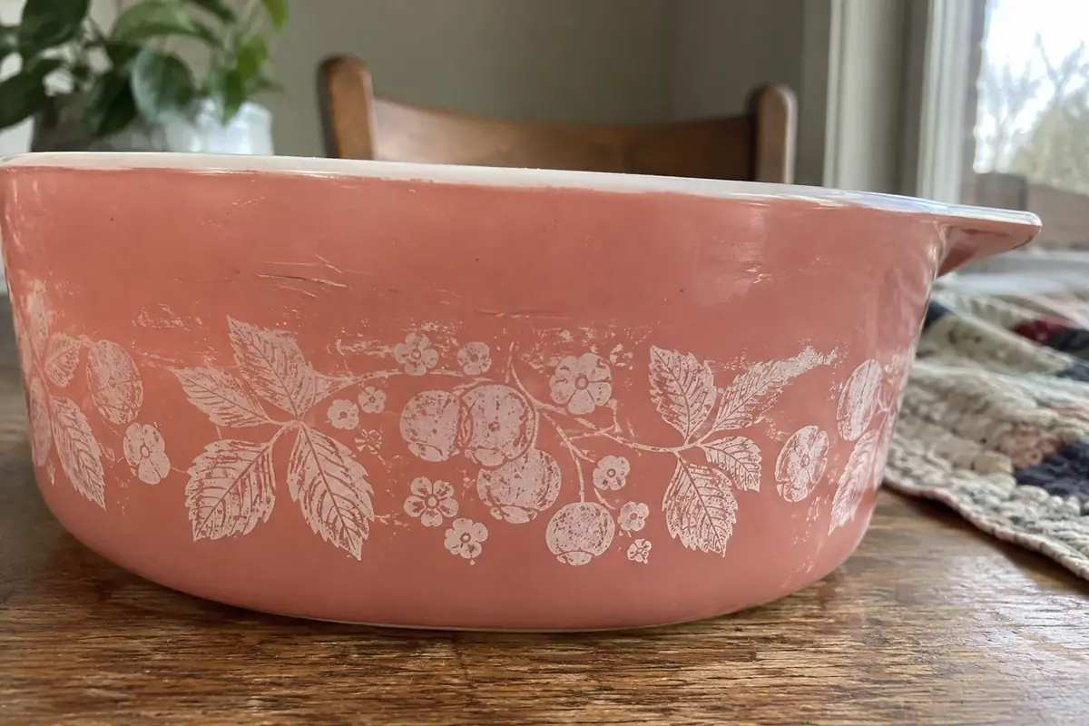 Close-up of a white berry-and-leaf print on a pink Pyrex dish, with fine scratches near the rim