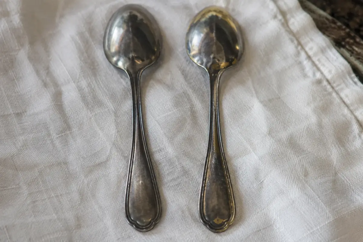Two teaspoons side by side, one evenly worn sterling, one plated with yellow metal showing at the bowl tip
