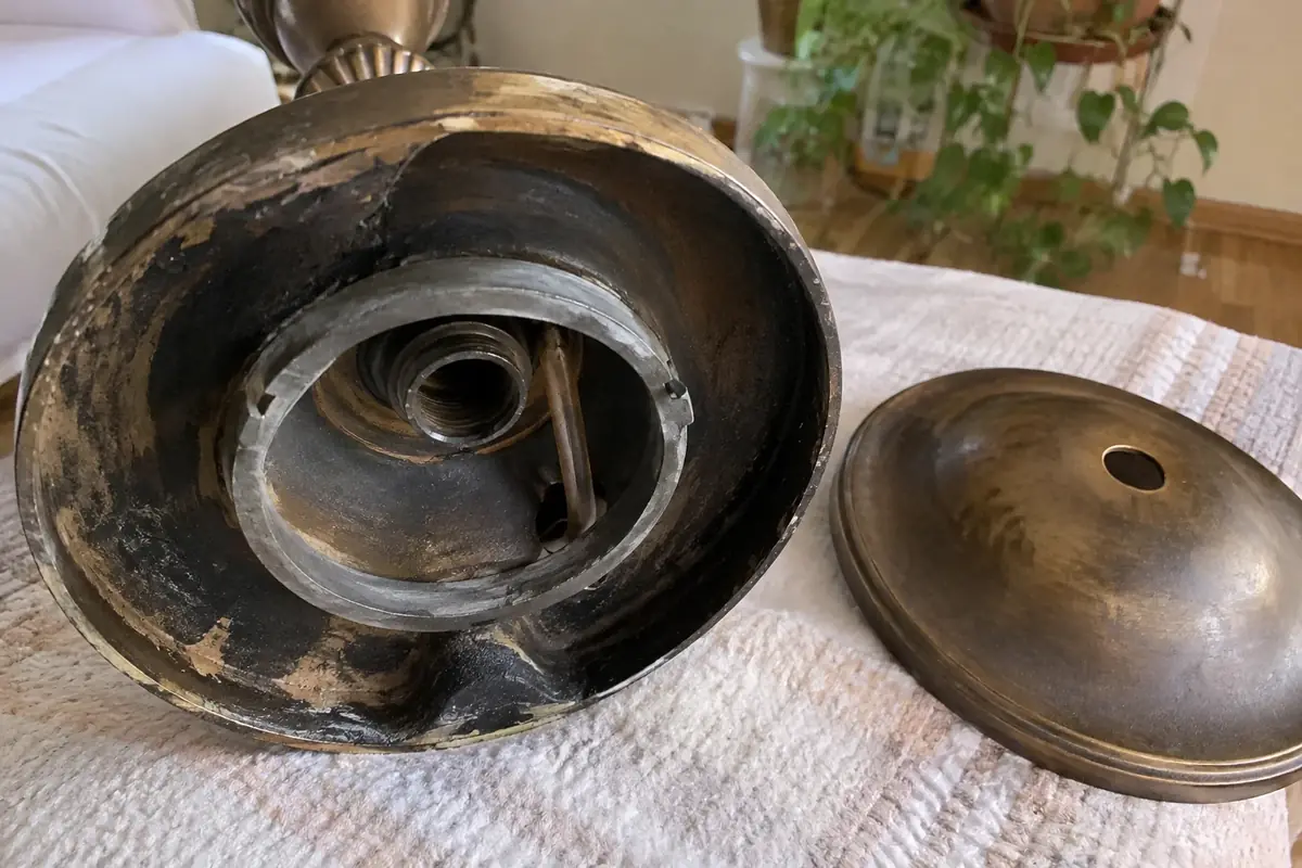 The underside of a dark bronze-toned lamp base with the cap lifted, showing a dull grey metal ring inside the hollow base