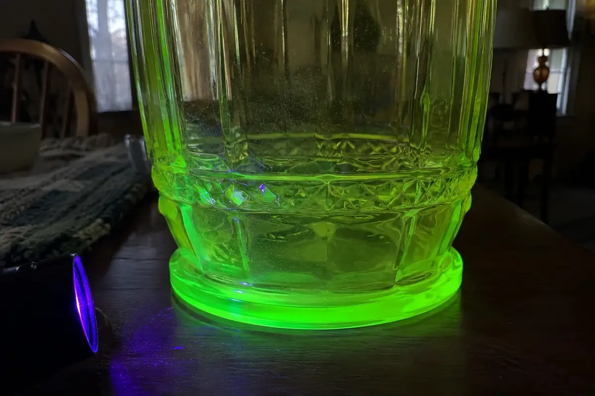 Base of a yellow-green glass pitcher glowing bright green under a black light in a dark room