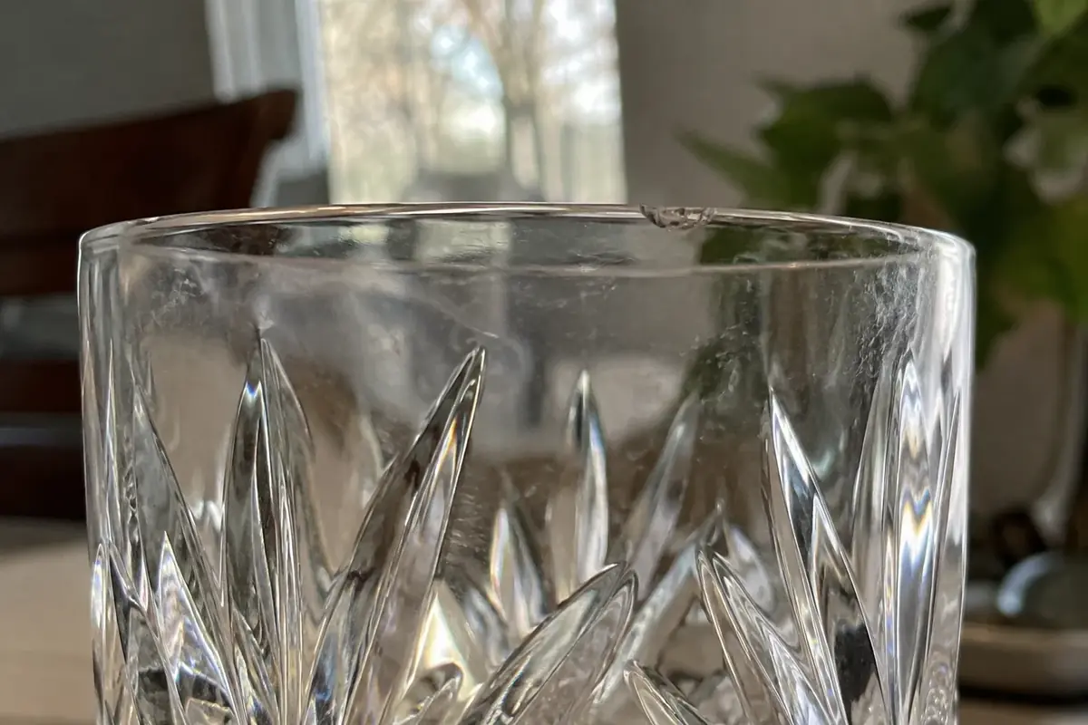 Close view of a cut-crystal tumbler rim with a small chip and light scratches on the diamond cuts
